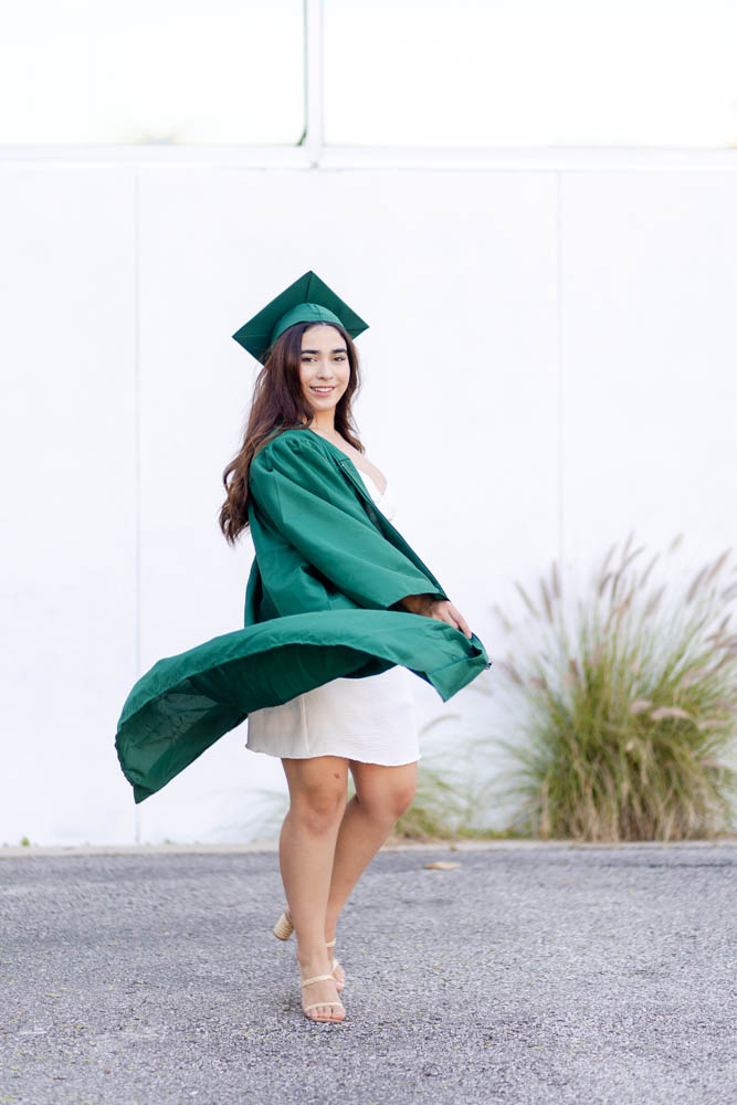 girl high school senior swirling in Dunedin Florida wearing a green cap and gown